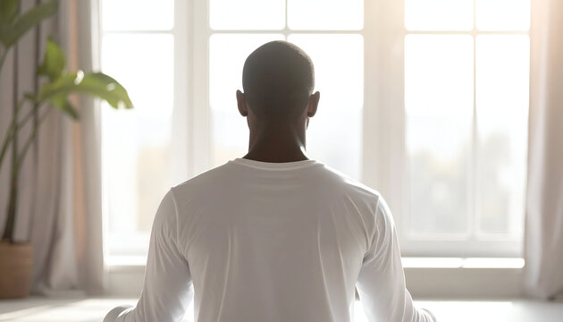 Man meditating peacefully in a serene white room with natural light. - Powered by Adobe
