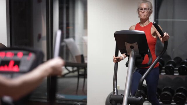 Mature woman engages in workouts using an elliptical machine at a gym, focusing on fitness and strength training routines.