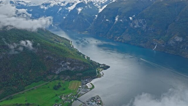 Aerial view of Aurlandsfjord seen from high above Stegastein, Norway. Deep blue fjord winds between steep mountains and green valleys under low drifting clouds.