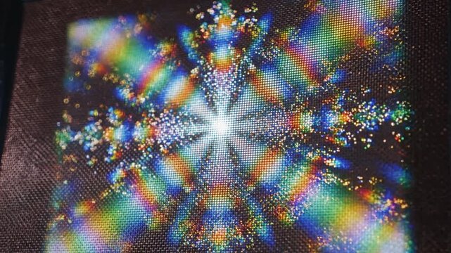 Close-up of a colorful crystal-like object with a starburst pattern and rainbow hues on a dark background with a shallow depth of field.
