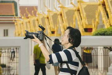 Person with short hair and glasses is taking photo with DSLR camera in temple setting, featuring ornate golden architecture. scene conveys sense of focus and cultural exploration