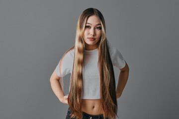 Young woman with long straight hair wearing white crop top standing with hands on hips looking at...