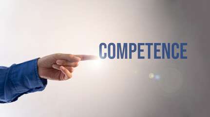 A hand pointing to the word "competence" on a gray background. Concept of someone being competent or skilled in a particular area