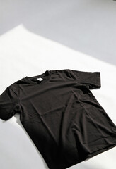 A black t-shirt lies crumpled on a white surface in natural light