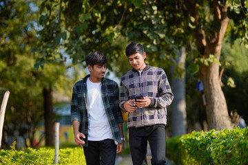 Obraz premium two indian teenagers boys looking smartphone and discussing at garden