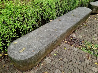 Stone bench in public park made from solid rock, long rectangular seating design outdoors, natural texture surface, urban landscape furniture, daylight scene.