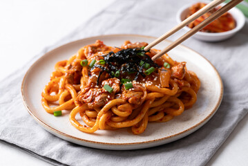 Stir fried Udon noodle with kimchi cabbage, pork, spring onion, sesame seed and seaweed on plate eaten by chopsticks
