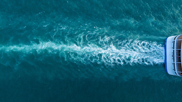 a ship's white wake trail on the deep blue ocean surface. Minimalist water texture with foaming waves left behind by a vessel, featuring copy space for text.