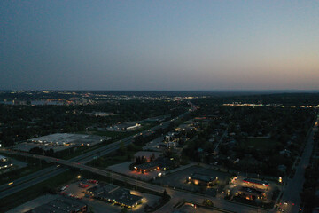 Fototapeta premium Aerial view of barrie, ontario, at dusk, showing residential and commercial areas, a highway with vehicle light trails, and the glowing city skyline along kempenfelt bay on lake simcoe