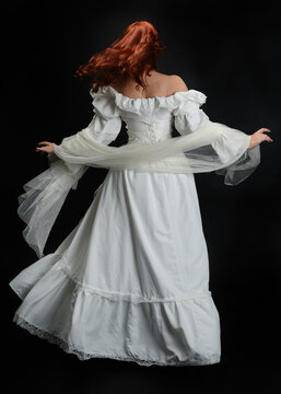 Full length portrait beautiful female model, red hair, wearing antique white historical ghost bride wedding dress gown. standing pose back view, Isolated figure on dark studio background