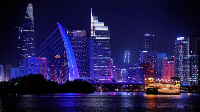 Night view of Bitexco Tower, colorful buildings, Bason bridge and Saigon river in Ho Chi Minh city, tourist boats and cruises on Saigon river