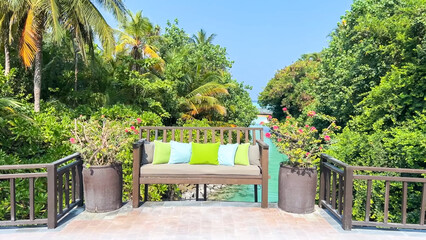 Outdoor wooden bench with colorful pillows overlooking a tropical canal