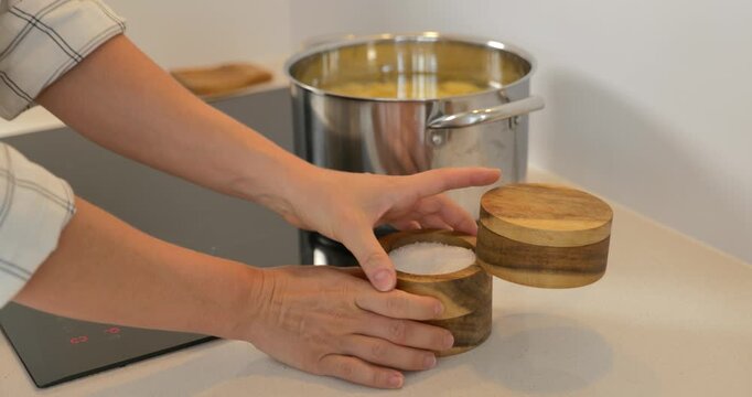 Woman boiling potatoes on an induction cooktop, stirring foamy water