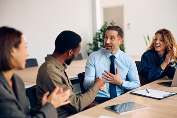 Fototapeta premium Happy businessmen shaking hands after successful meeting in office while their female colleagues are applauding them.