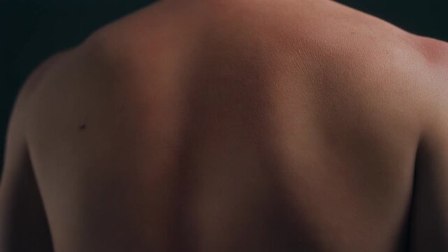 Detailed close up shot of a young adult male's bare, muscular back, highlighting the healthy, tanned skin texture and subtle, defined muscle
