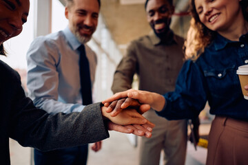 Close up of entrepreneurs celebrating their business success while joining hands in unity in office.
