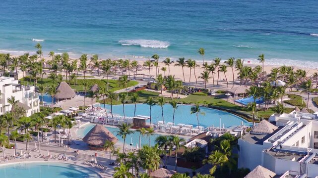Aerial view of Hard Rock Hotel in Punta Cana, Dominican Republic, with palm-lined pools, beachfront resort buildings and turquoise Caribbean waters along sandy coast. Wide shot.