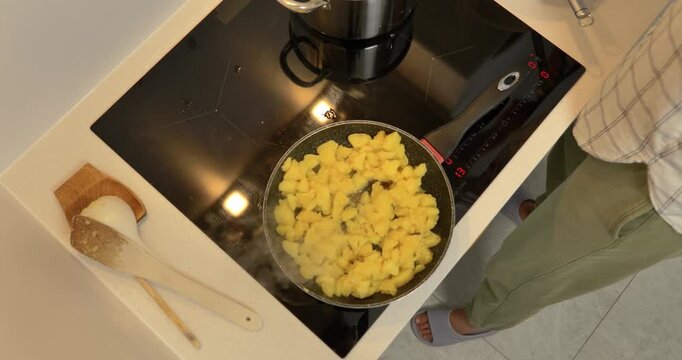 Close-up of hands frying boiled potato pieces in a pan on an induction cooktop