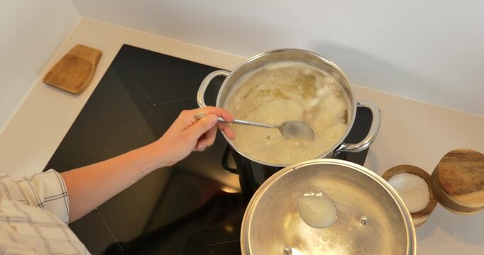 Woman boiling potatoes on an induction cooktop, stirring foamy water