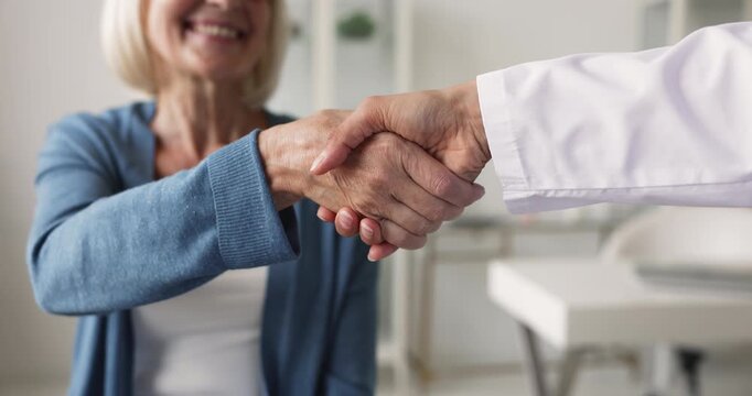 Closeup of smiling middle age woman and nurse shaking hands, representing trust between patient and doctor, satisfaction with professional medical and health care services, successful consultation end