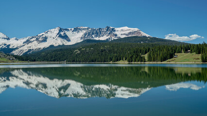 Obraz premium Mountain Lake Reflection with Snow-Capped Peaks and Evergreen Trees
