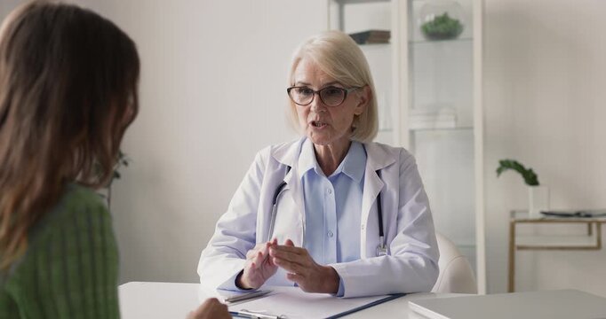 Smiling middle-aged woman doctor talking with patient, gives professional advice, discussing treatment, explains further procedure, share good news, supporting or reassuring during her visit in clinic