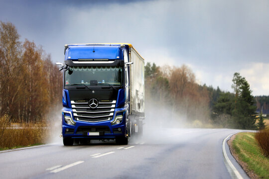 Blue Mercedes-Benz Actros Freight Truck Transports Goods along Wet Highway on a Rainy Day. Copy Space.