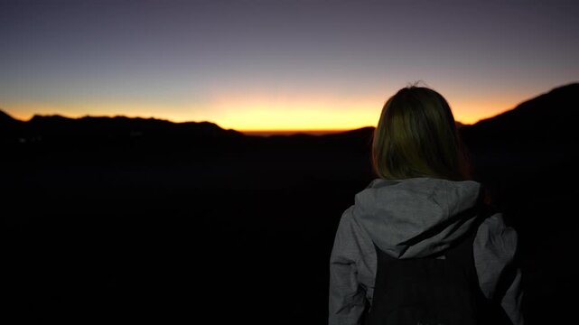 Happy female traveler atop Mt Bromo at twilight waiting for sunrise, Indonesia