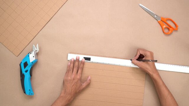 Hands crafting with cardboard using tools on flat surface