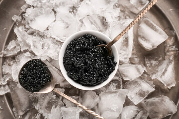 Bowl of delicious black caviar with spoon and ice cubes on tray, top view