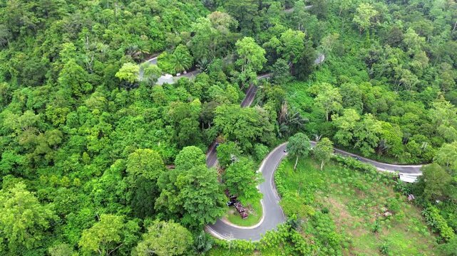 Aerial video shows many cars on a winding and uphill road in a green mountain full of trees.