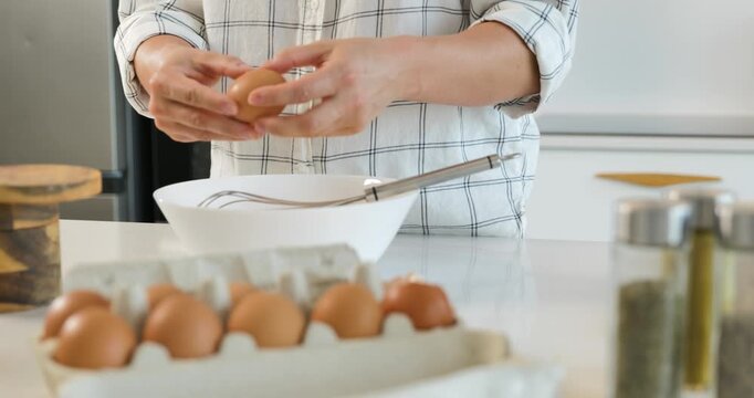 Hands cracking fresh eggs and whisking omelette mixture in a bowl on kitchen counter