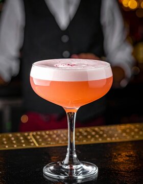   C&oacute;ctel rosado con espuma cremosa en copa elegante sobre barra.
