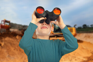 A young boy is looking through binoculars at a construction site