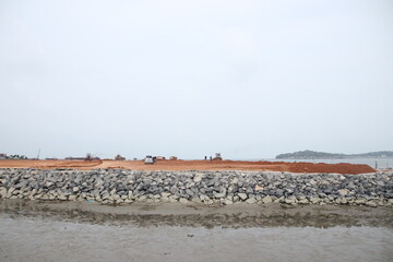 yellow tractor and heavy construction machinery transport equipment across a rural field,  across a beautiful landscape of sand, sea, and sky near a boat on the coast