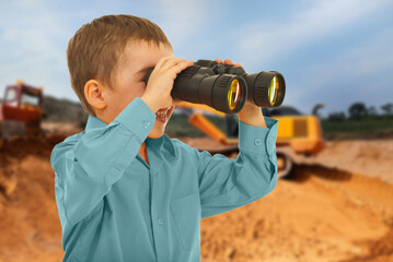 A young boy is looking through binoculars at a construction site
