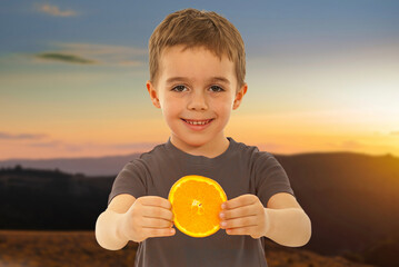 A young boy is holding an orange in his hand and smiling