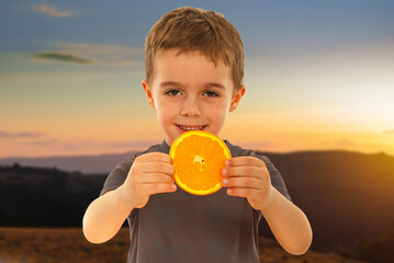 A young boy is holding an orange in his hand and smiling