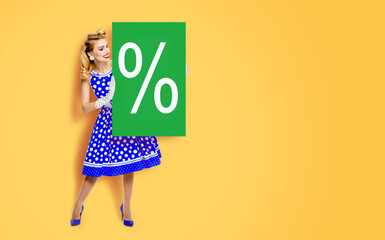 Beautiful woman in pinup blue dress pointing show board with percentage % sign. Full body pin up cute girl hold advertise offer promo, isolate yellow background. Spring season sale ad concept image