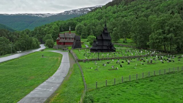 Path leading through open fields toward an iconic wooden church. Borgund Stave Church sits quietly in a green Norwegian valley.