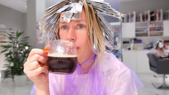 Moscow, Russia, 24.04.2025 Caucasian woman enjoying coffee during hair highlighting treatment at salon, taking selfie video