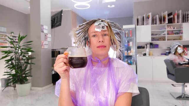 Moscow, Russia, 24.04.2025 Woman drinking coffee at beauty salon during hair foiling highlighting procedure for hair coloring footage