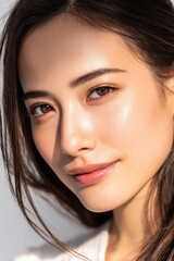 Fototapeta premium A young Asian woman with clear, glowing skin softly in natural light, with a clean background highlighting her skin and healthy complexion.