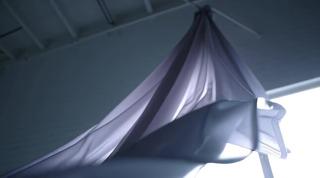 A flowing fabric hangs from the ceiling, gently swaying in the breeze, creating a dynamic display of texture and shadow in an indoor setting.