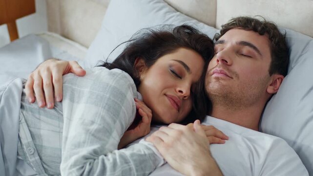 Man woman Caucasian couple lying together bed bedroom sleeping home hugging love cozy eyes closed slumber nap relaxing rest daydream sweetheart honeymoon beloved boyfriend girlfriend tenderness cuddle