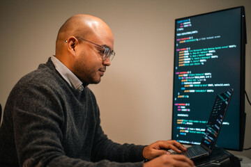 Male programmer wearing glasses works late at night with green code reflecting on his lenses focusing on software development coding and cybersecurity analysis.