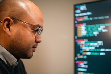 Male programmer wearing glasses works late at night with green code reflecting on his lenses focusing on software development coding and cybersecurity analysis.