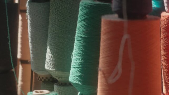 Zoomed-out view of colorful yarn cones in shades of green, orange, turquoise, and more, lined up with loose threads in a traditional textile weaving mill.