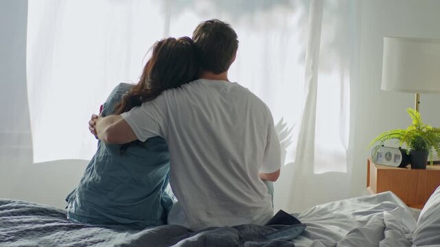 Back view Caucasian man woman couple sitting on bed hugging in bedroom at home boyfriend hug girlfriend together cozy hotel tenant cuddle bond loving tenderness sweetheart harmony wife husband feeling