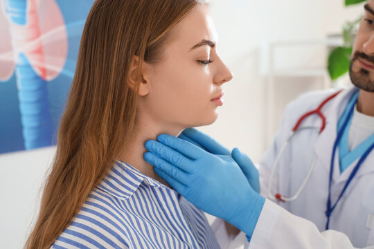 Male endocrinologist examining woman's thyroid gland in clinic, closeup